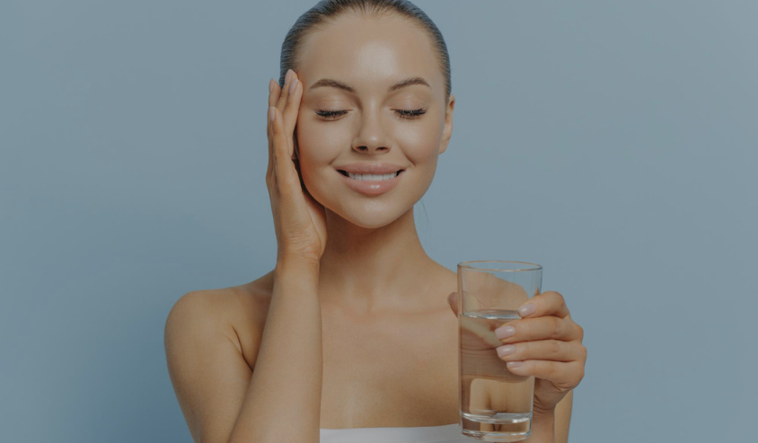 The image shows a woman with a serene expression, holding a glass of water. She appears to be enjoying the refreshing and healthy properties of the water.