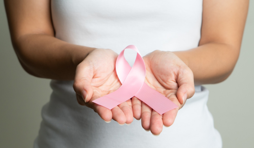 Hands gently cupping a pink breast cancer awareness ribbon, a symbol of care and support.