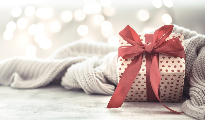 Cozy holiday gift box with red ribbon on a knitted blanket