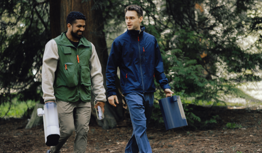 Two men walking in a wooded area, one carrying a Bluevua ROPOT-Travel.