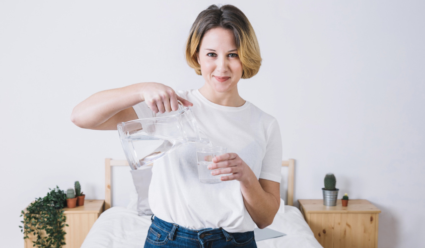 Person pouring filtered water into a glass at home